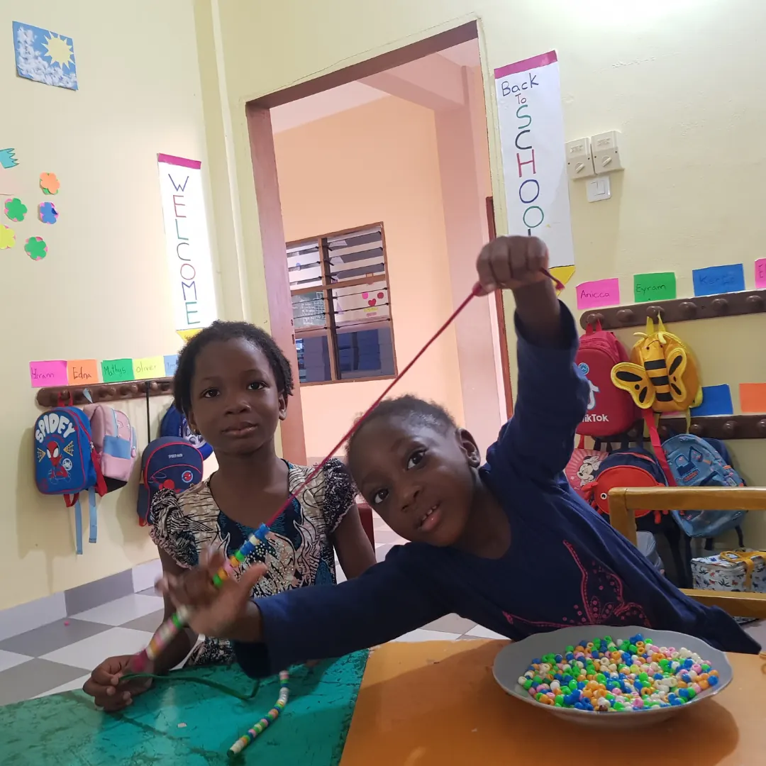 Two girls playing with a bowl of colourful beads in a bright classroom